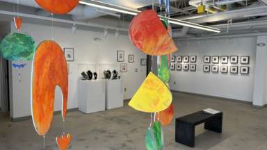 Gallery with several artists work displaying including colorful hanging shapes, framed works on paper