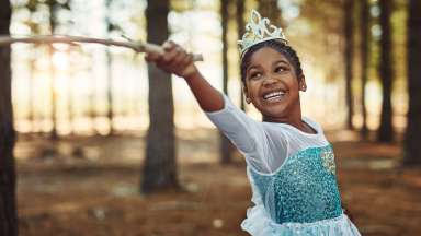 Little girl dressed in princess costume wearing crow waving wand