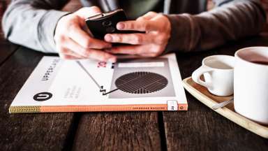 Hands holding a cell phone while sitting at a table with coffee