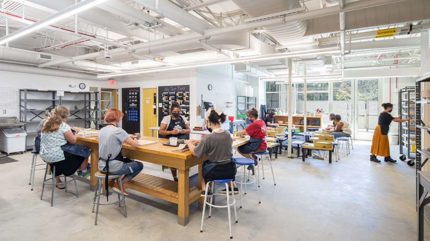 People working at tables and pottery wheels in the pottery studio at Pullen Arts Center