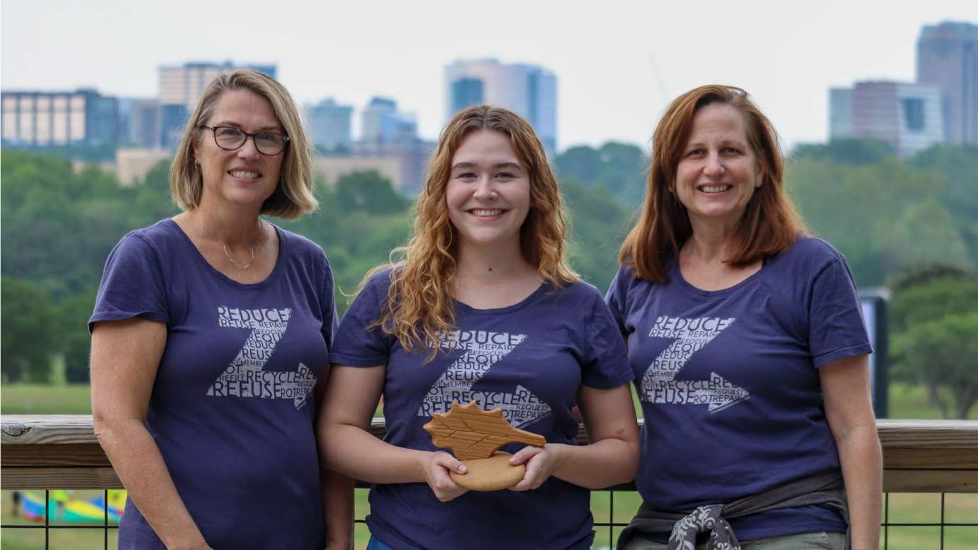 Three members of Toward Zero Waste pose with award with Raleigh skyline in background.