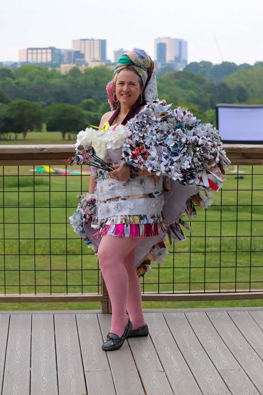 Woman in outfit made of trash stands in front of Raleigh skyline
