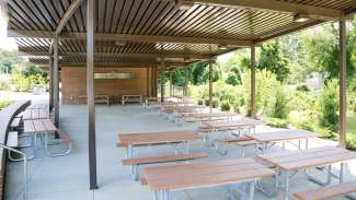 A large, open outdoor picnic shelter with over a dozen tables