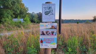 Sign for ecoEXPLORE on post in nature preserve surrounded by grass and trees