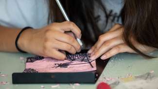 A teen etches into a pink block to be used for printing