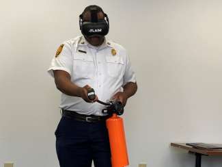 Lt. Hubbard with VR headset on facing camera and holding FLAIM extinguisher prop