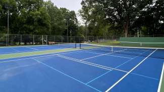 Two outdoor tennis courts with backboards and lighting