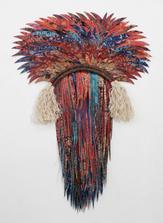 Two dimensional fiber sculpture with feather like fabric making a head-like shape in blues and reds.