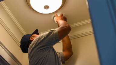 A person installing a smoke alarm next to a light on the ceiling