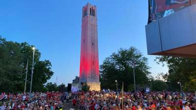 The belltower on NCSU campus is lite red with crowds celebration around it.