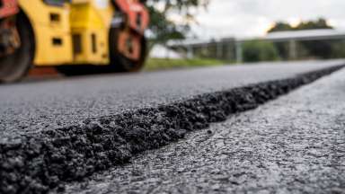 Close up photo of asphalt with construction equipment seen in background
