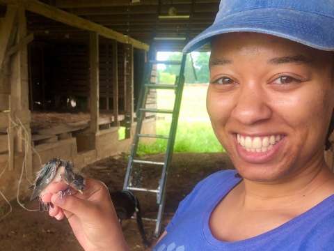 Woman smiling with barn swallow chick resting on her hand