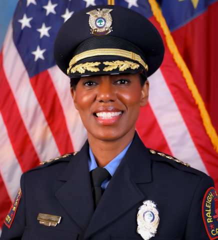Raleigh Chief of Police Estella D. Patterson smiling in front of NC State flag and American Flag