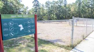 An outdoor, fenced in dog park at Buffaloe Road next to a sign with dog park rules